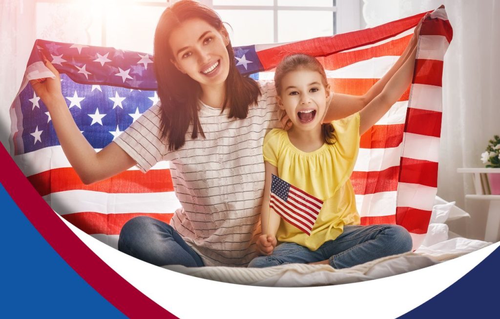 Image of a mother and daughter holding an American flag together on their couch.